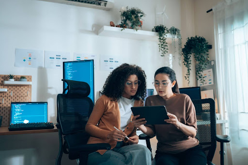 Two women sit in an office, using Software-as-a-Service on a tablet.